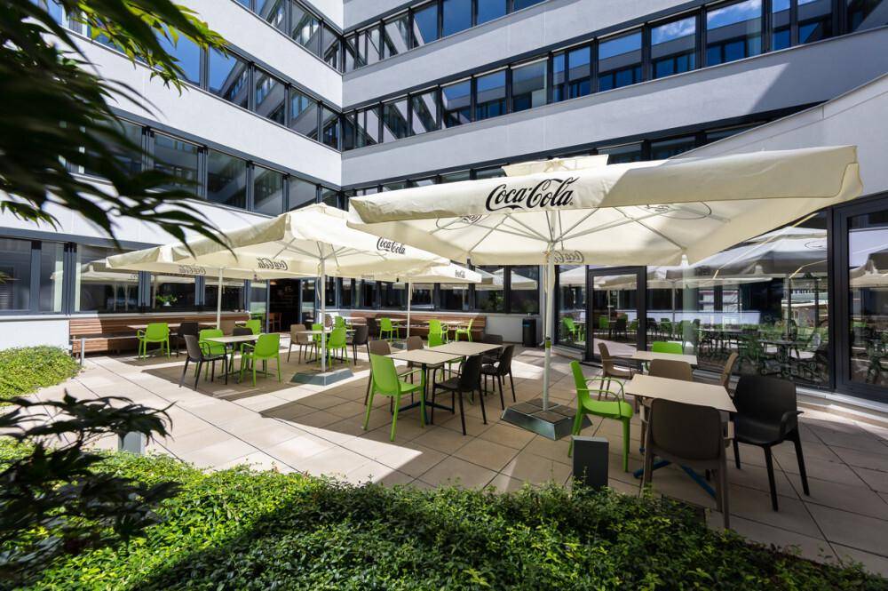 Gemütlicher Außenbereich mit Sonnenschirmen und Sitzgelegenheiten in einem begrünten Innenhof des Bürokomplexes.