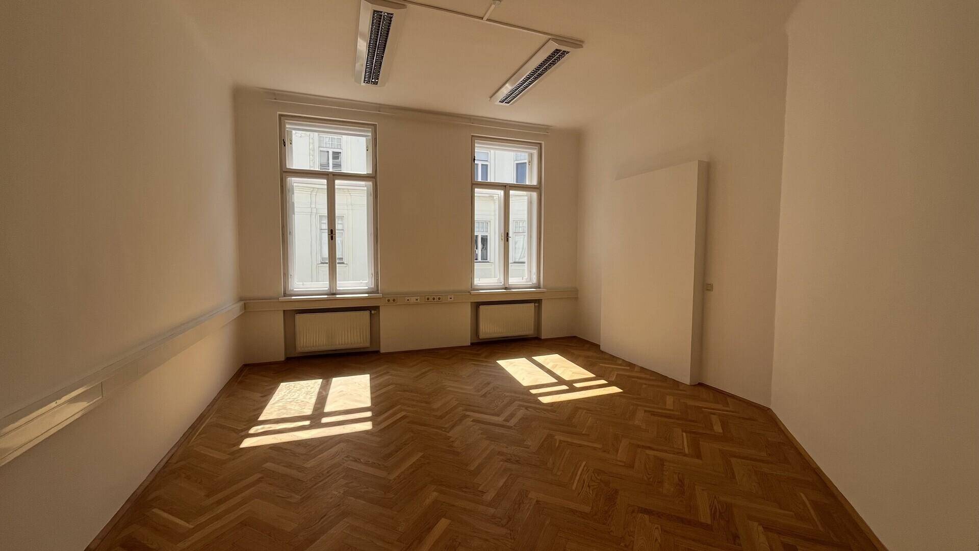Helles Büro mit Fischgrätparkett, zwei Fenstern und direkter Sonneneinstrahlung auf den Boden.