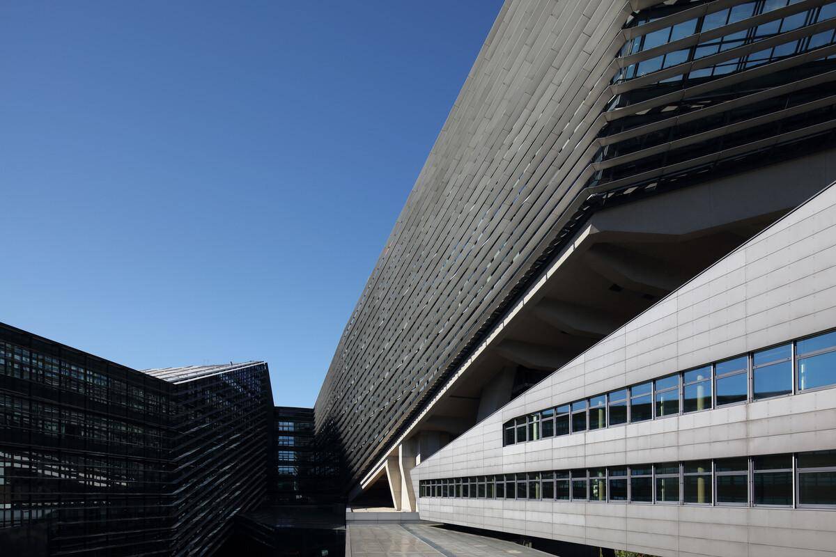 Beeindruckende moderne Architektur mit schrägen Linien und einer Kombination aus Glas- und Steinfassaden unter blauem Himmel.