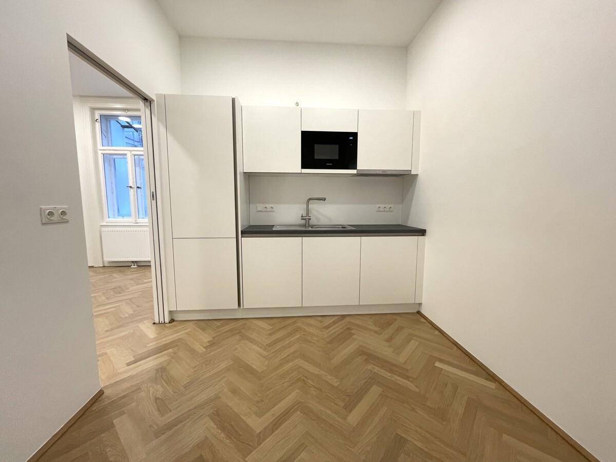 Moderne Küchenzeile mit weißen Schränken, Spüle und integrierter Mikrowelle in einem hellen Raum.