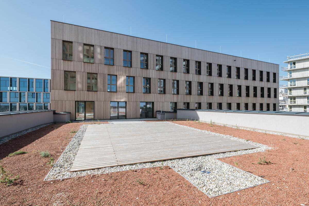 Große Dachterrasse mit Holzboden und Kiesflächen, umgeben von moderner Architektur und blauem Himmel.