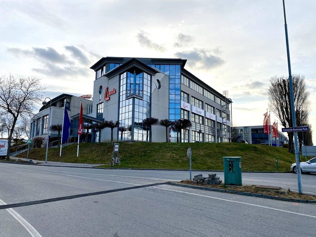 Modernes Bürogebäude im Concorde Business Park mit auffälliger Glasfront und einer begrünten Böschung davor.
