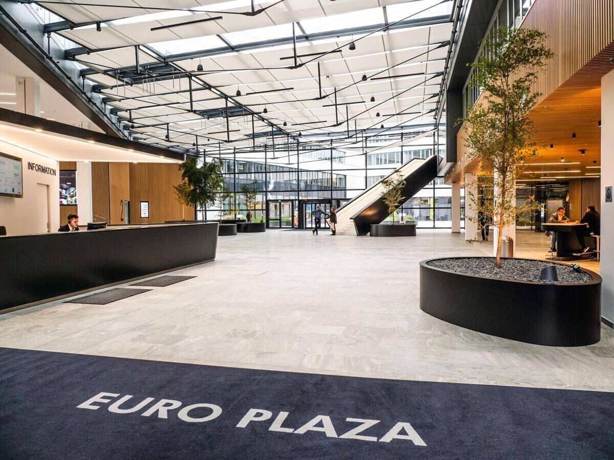 Geräumiger Empfangsbereich mit Informationstheke, Rolltreppe und "EURO PLAZA" Teppich.