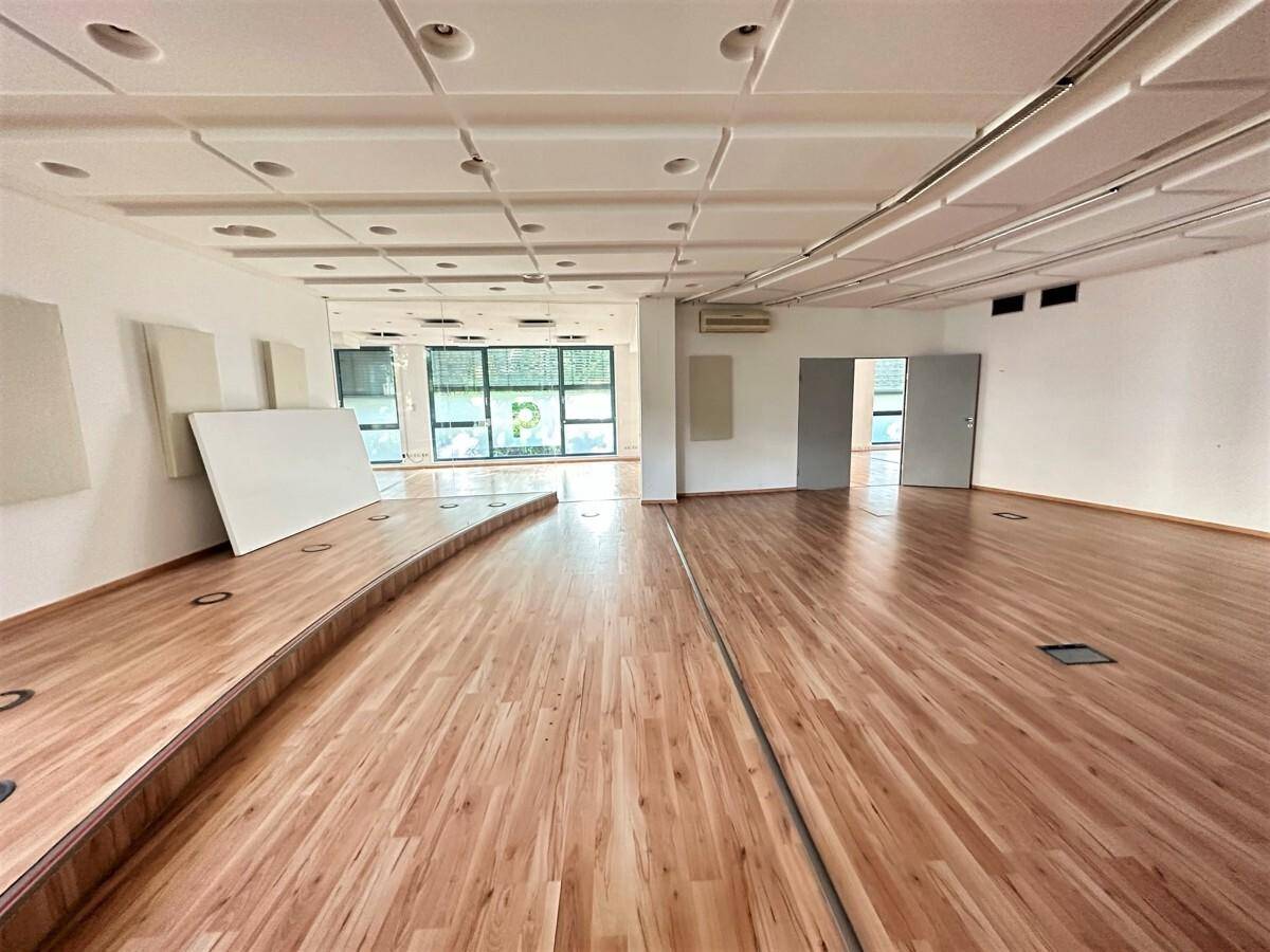 Großer, offener Raum mit Holzboden, einer erhöhten Plattform und abgehängter Decke, ideal für Veranstaltungen oder Kurse.
