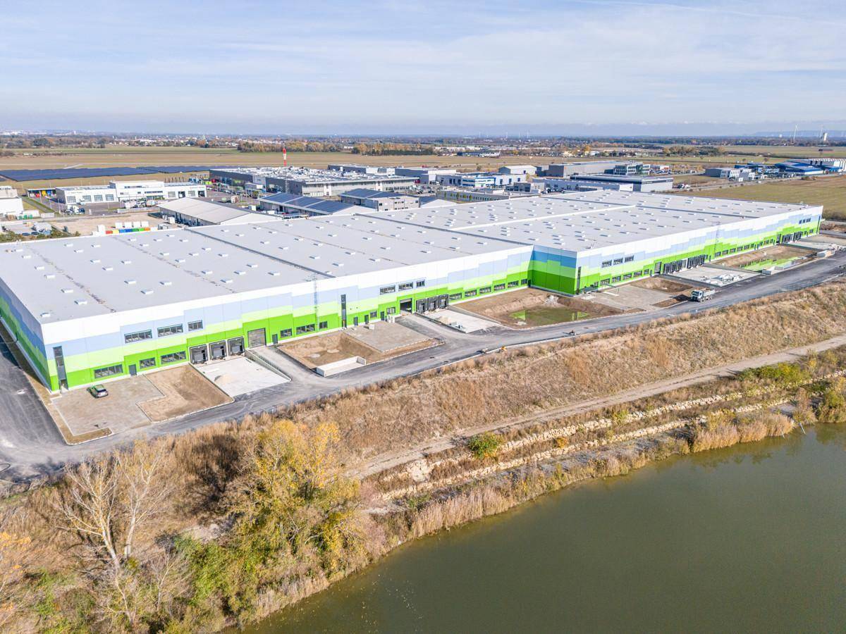 Luftbild des großen Logistikzentrums mit angrenzendem Fluss oder Kanal und weiten Feldern.
