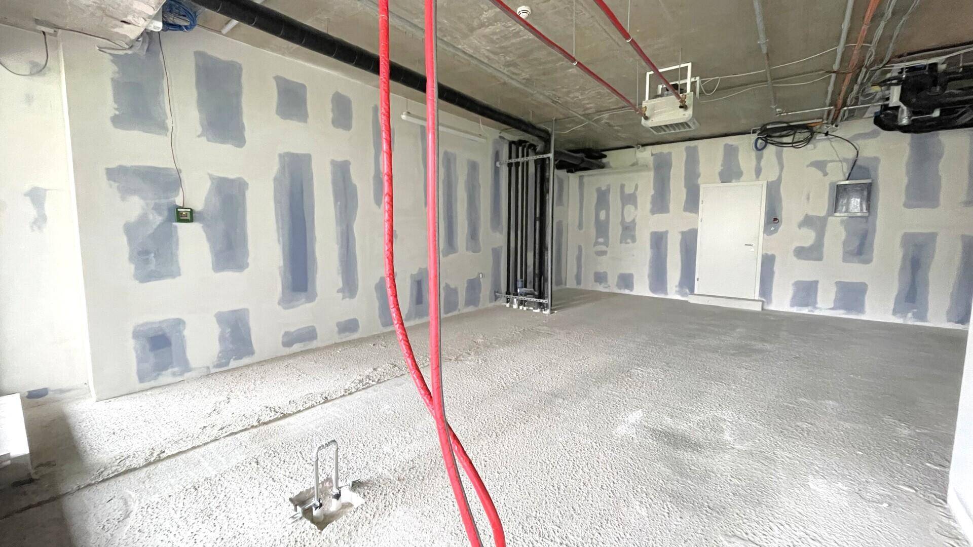 Innenansicht eines Gewerberaums im Rohbau mit sichtbaren roten Leitungen und unfertigen Wänden, die auf den Ausbau warten.