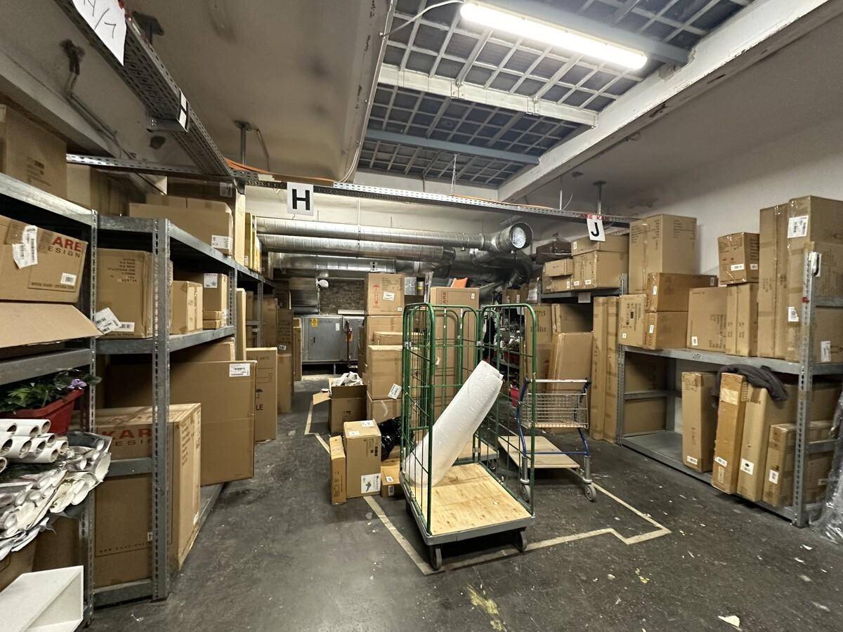 Lagerraum mit Regalen voller Kartons, industrieller Beleuchtung und sichtbaren Lüftungsrohren.