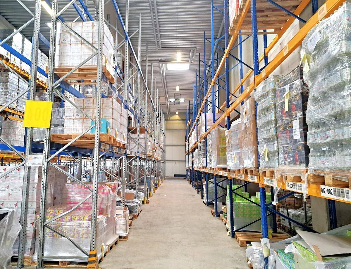 Langer Gang in einer modernen Lagerhalle mit hohen Regalen voller verpackter Produkte.