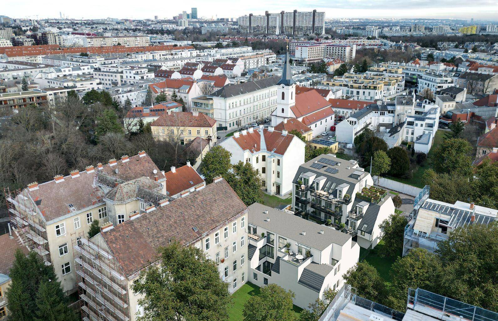 Luftaufnahme einer städtischen Umgebung mit einem neuen Wohngebäude und umliegenden Altbauten unter bewölktem Himmel.