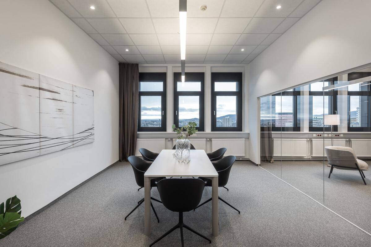 Heller Konferenzraum mit großem Tisch, bequemen Stühlen und weitem Ausblick durch die Fenster.
