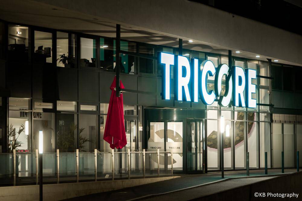 Eingangsbereich des Bürogebäudes bei Nacht mit leuchtendem Firmenlogo und moderner Glasfassade.