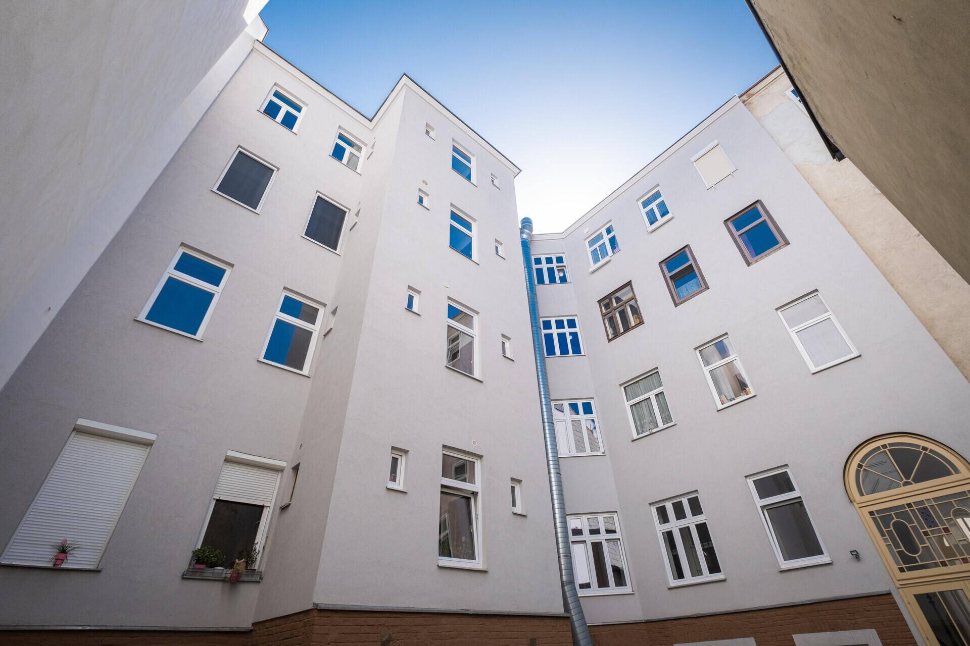 Innenhof eines Gebäudes mit vielen Fenstern und einer Entwässerungsrinne unter blauem Himmel.