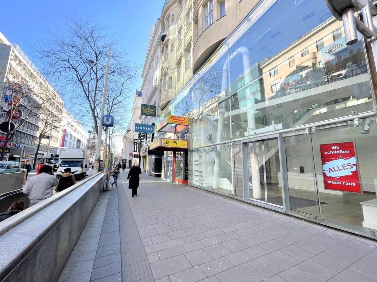 Weitläufige Straßenansicht mit moderner Glasfassade des Geschäftsgebäudes und Passanten auf dem Gehweg.