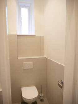 Separate Toilette mit Fenster, wandhängendem WC und hellen Fliesen an Wänden und Boden.