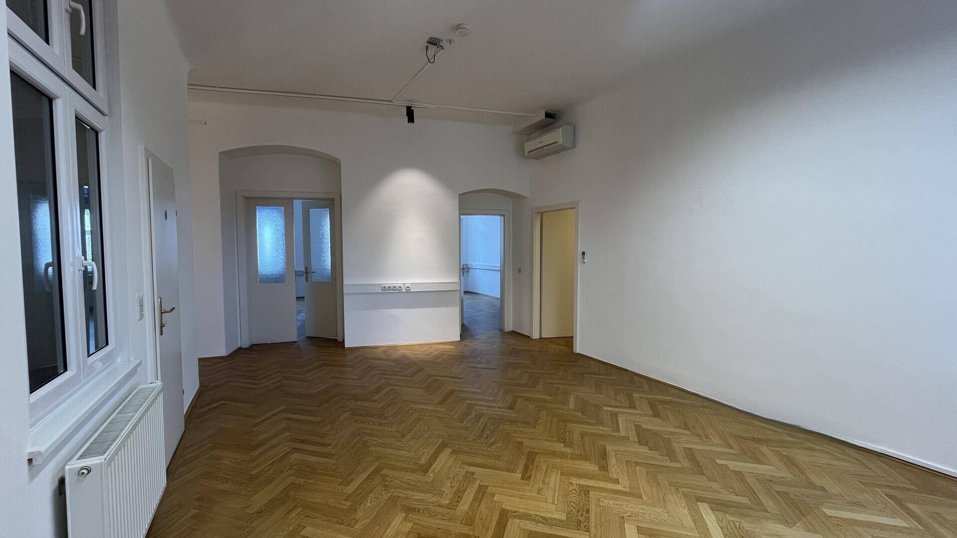 Großer Büroraum mit Fischgrätparkett, hohen Decken und Klimaanlage, gut erhalten.