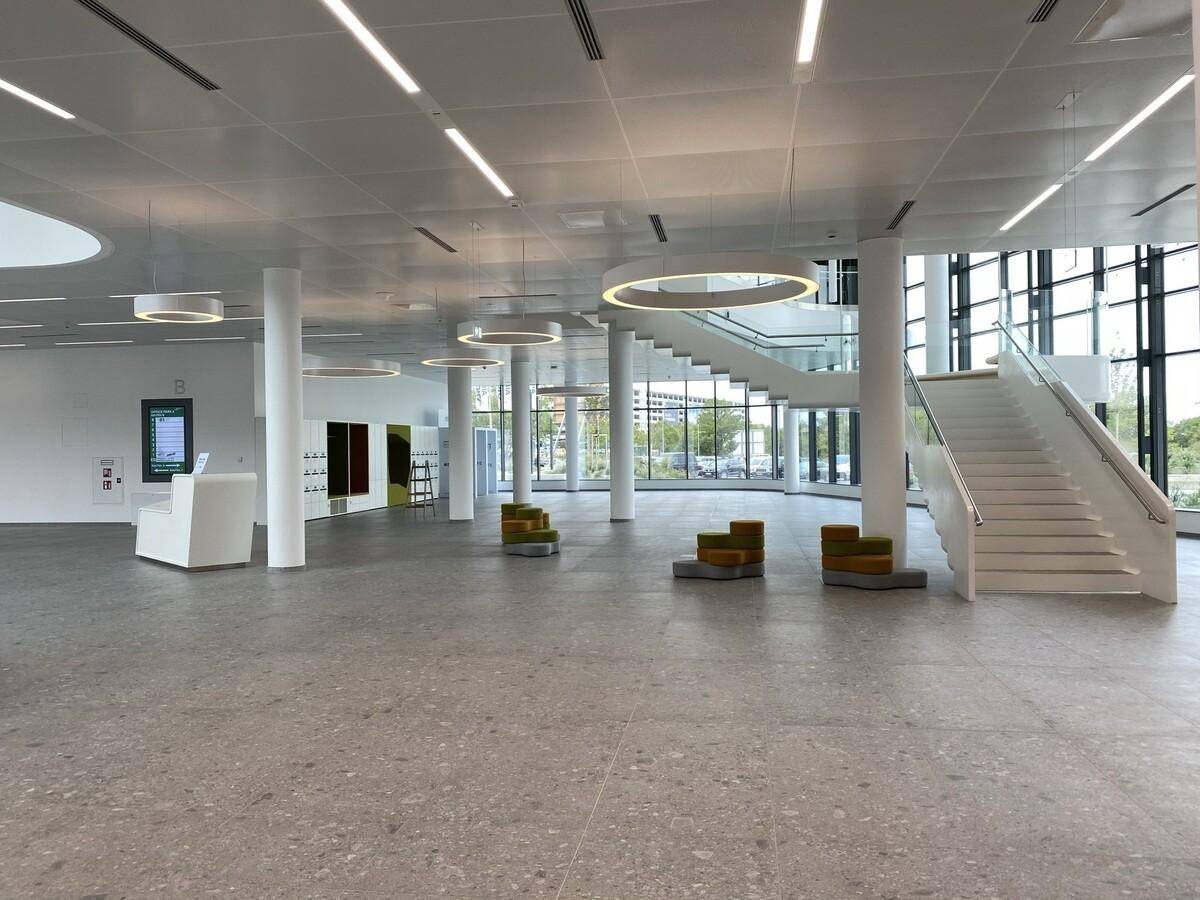 Geräumige Lobby mit moderner Treppe, hohen Decken und großen Fenstern.