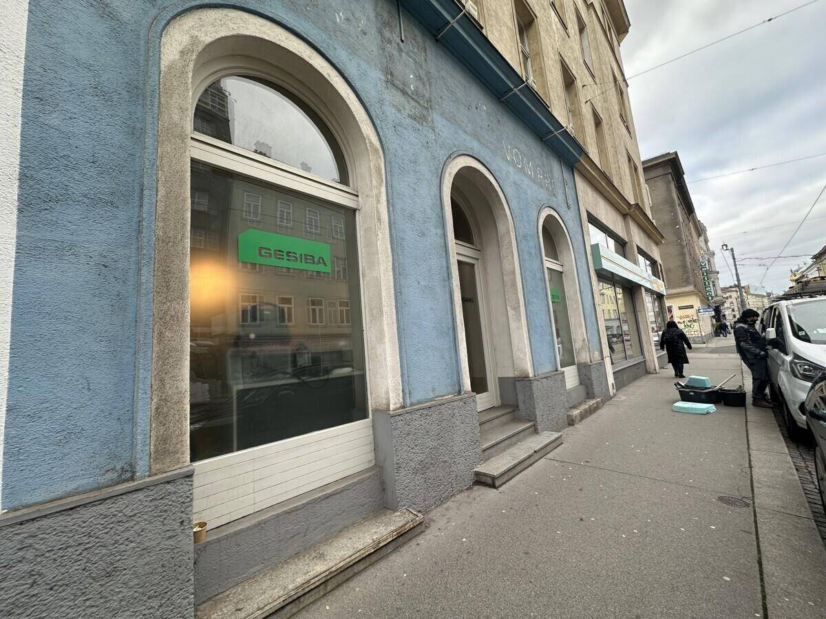 Nahaufnahme der blauen Gebäudefassade mit großen Bogenfenstern und einem Geschäftsschild an der Straßenseite.