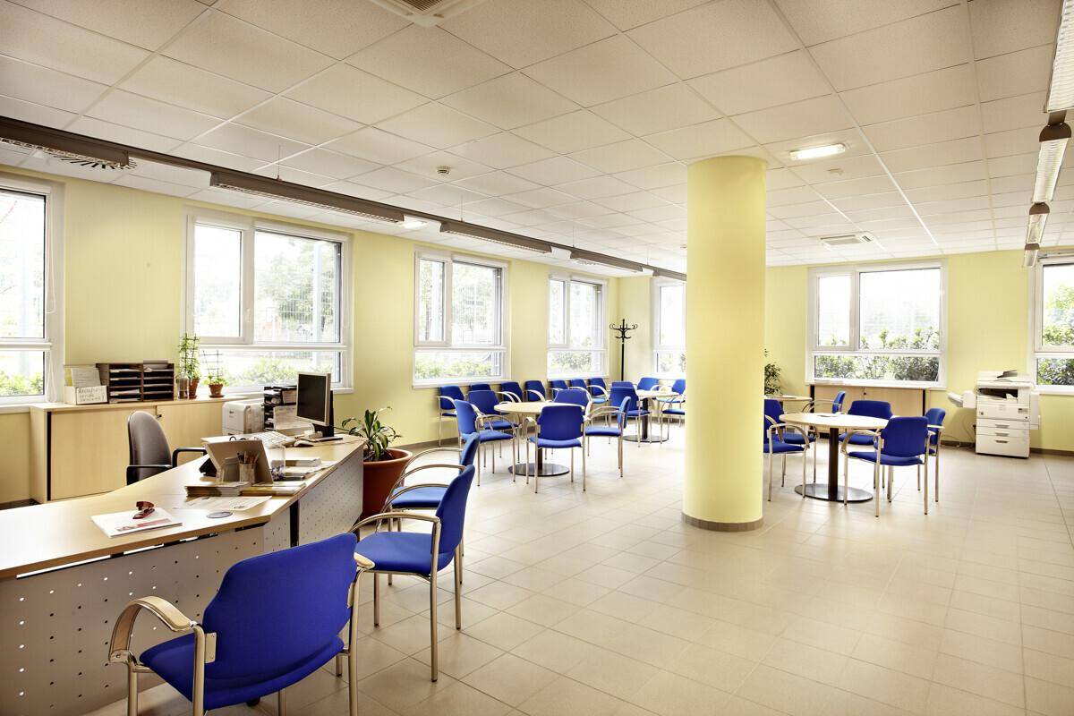 Heller Empfangsbereich oder Wartezone in einem Bürogebäude mit vielen Fenstern und blauen Stühlen.