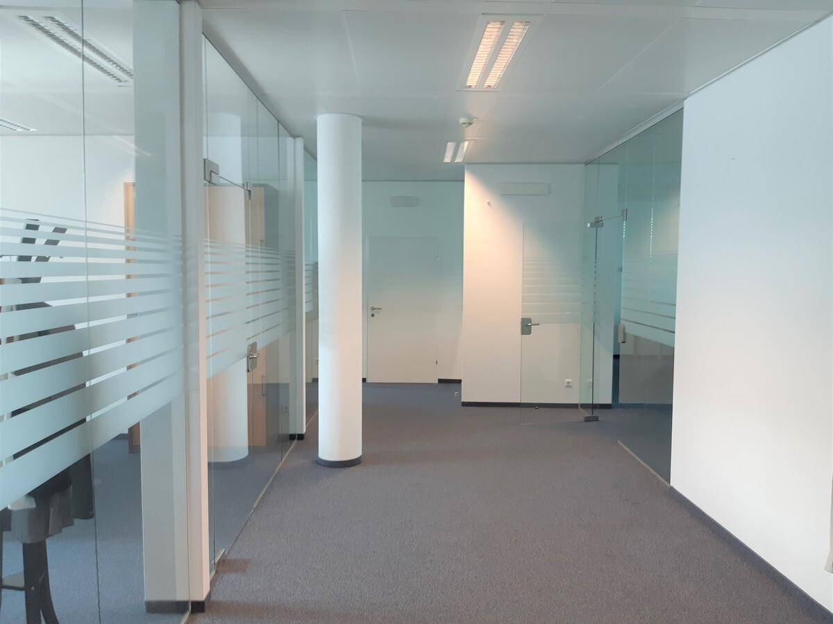 Modernes Büro mit Glaswänden und Teppichboden, das eine offene und helle Arbeitsumgebung bietet.