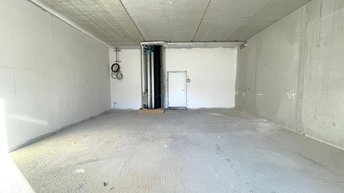 Großer, leerer Gewerberaum im Rohbauzustand mit Betonwänden und sichtbaren Installationen.