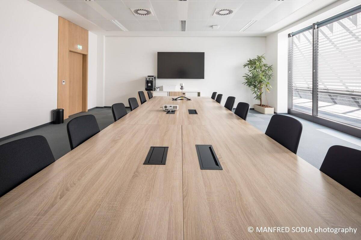 Großer Konferenzraum mit langem Holztisch, vielen Stühlen und einem großen Bildschirm.