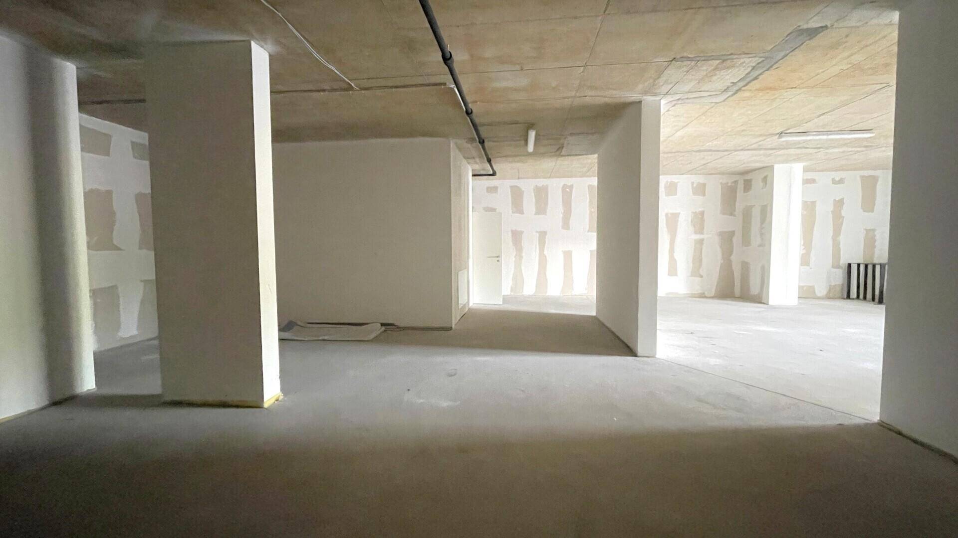 Großer, unfertiger Raum mit Betonboden und -decke, teilweise verputzten Wänden und sichtbaren Säulen.