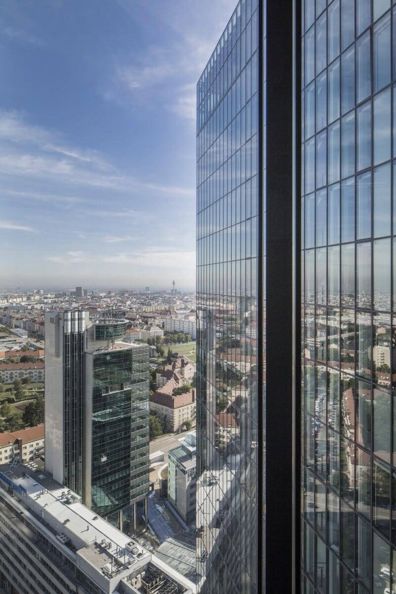 Panoramablick auf die Stadtlandschaft von einem modernen Hochhaus mit Glasfassade unter blauem Himmel.