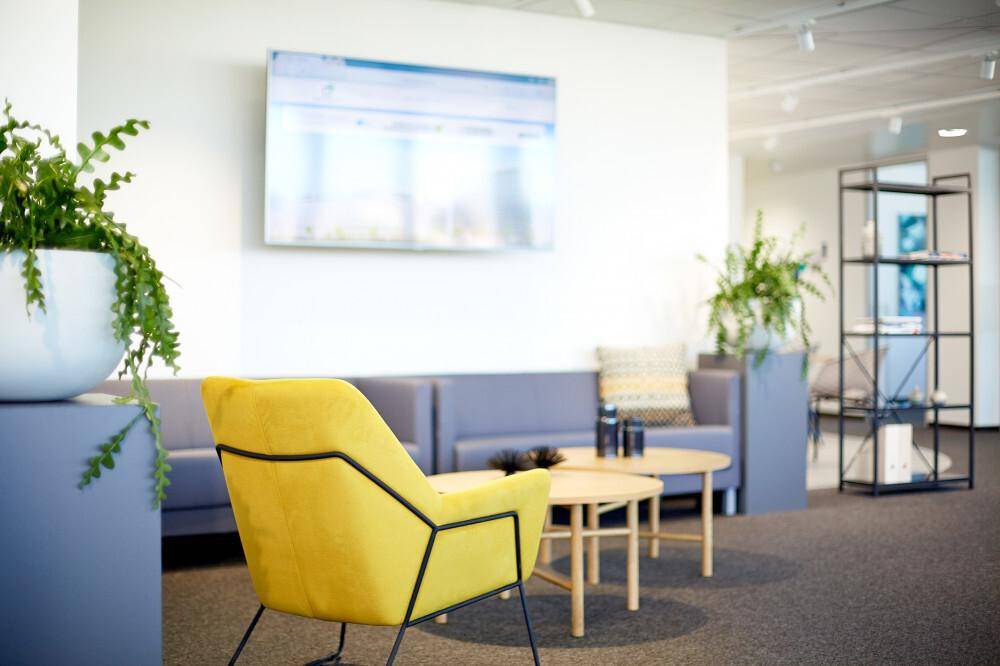Moderner Loungebereich mit bequemen Sofas, einem gelben Sessel und einem Flachbildschirm an der Wand.