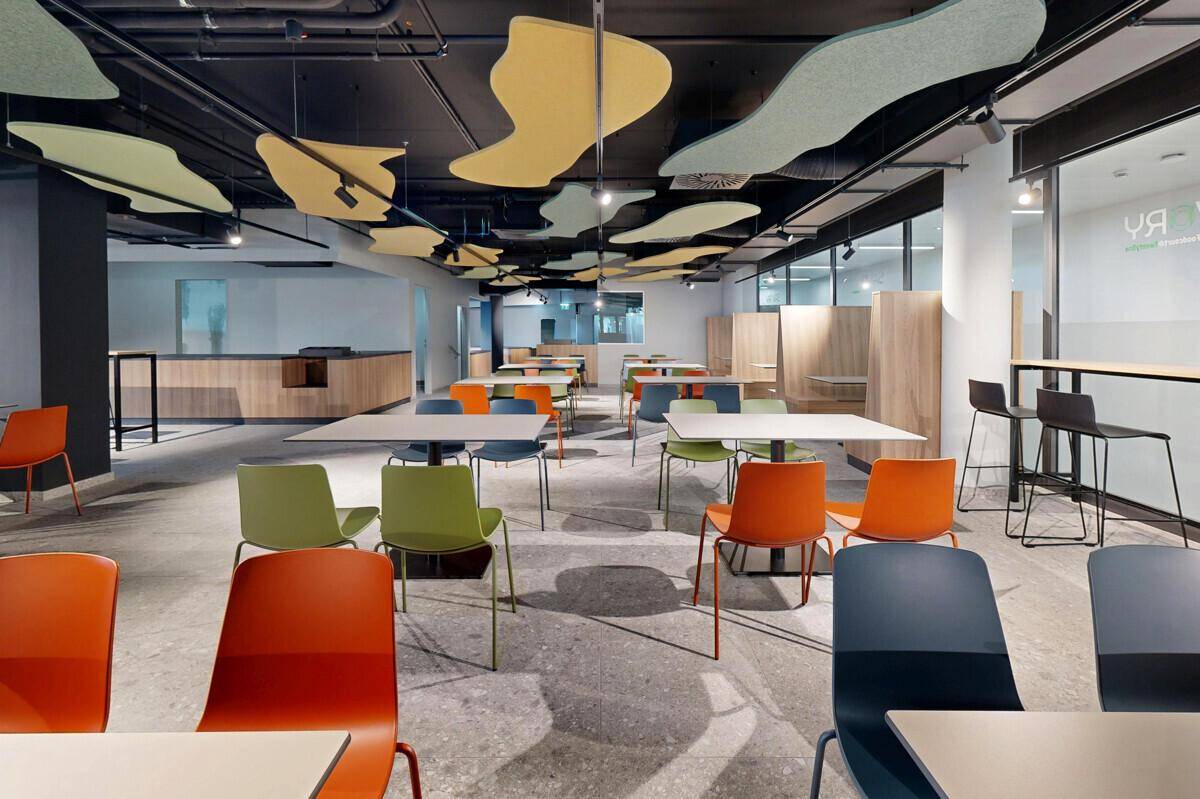 Moderne Cafeteria mit farbigen Stühlen, industriellem Decken-Design und Betonboden.