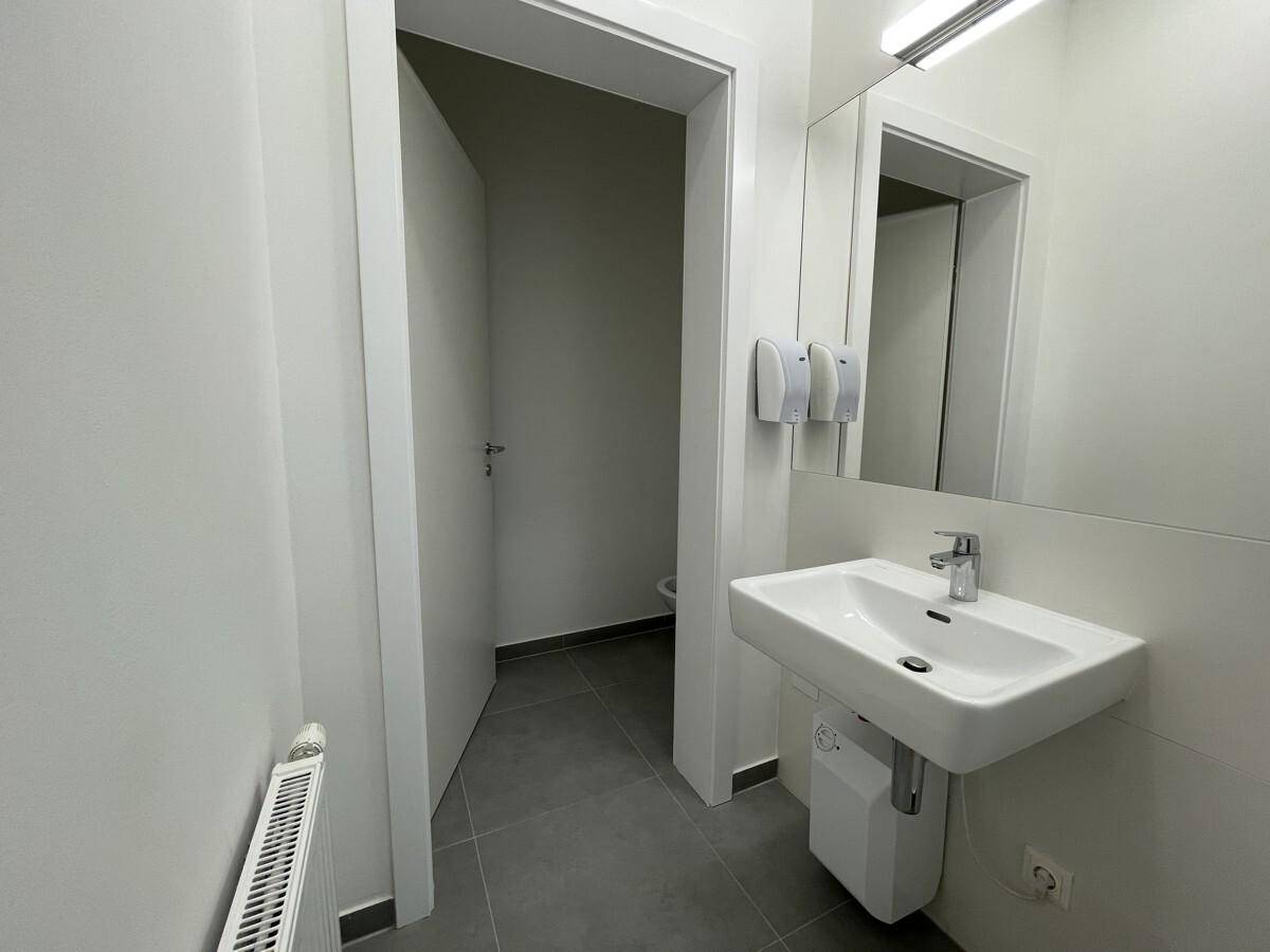 Modernes Badezimmer mit Waschbecken, Spiegel und Zugang zu einer separaten Toilette, ausgestattet mit Fliesenboden.