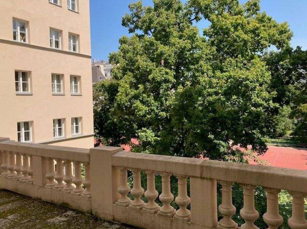Geräumiger Balkon mit steinerner Balustrade und Blick auf grüne Bäume und einen Sportplatz.