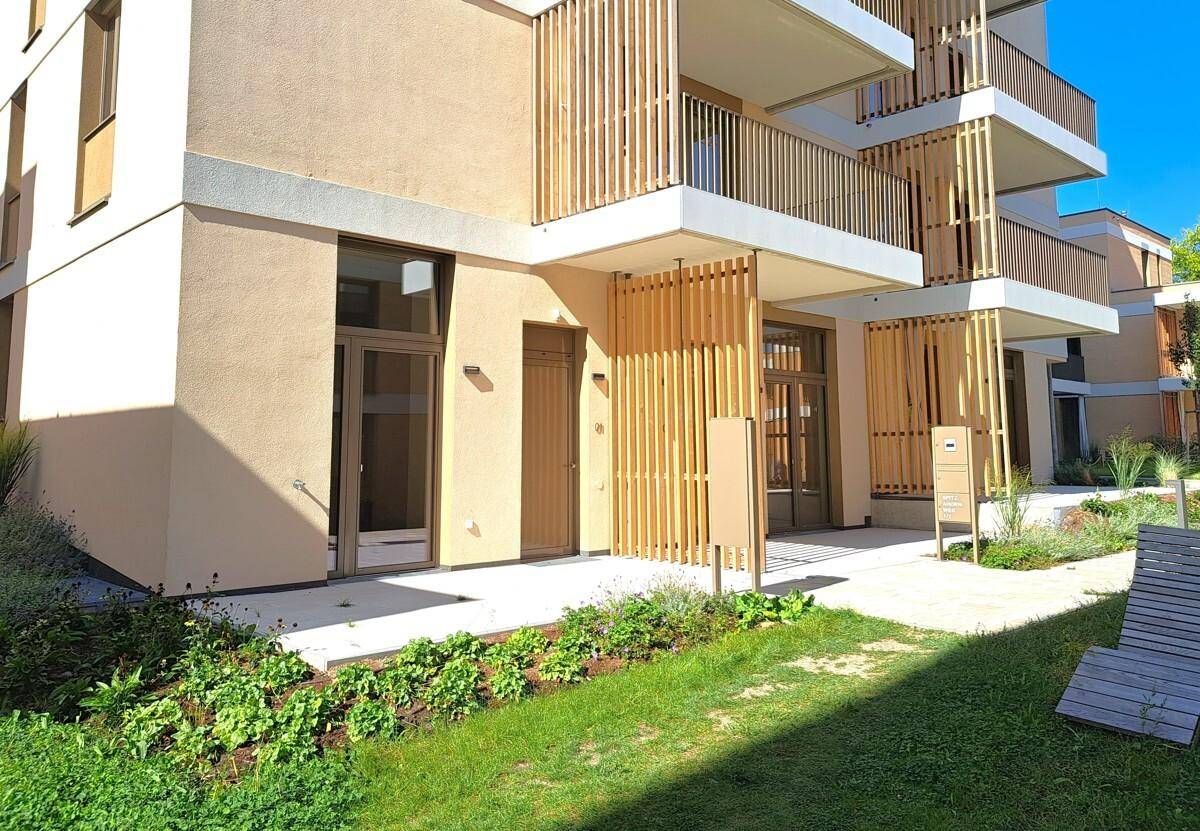 Moderne Gebäudefassade mit Balkonen, Holzlamellen und Zugang zu den Erdgeschosswohnungen.