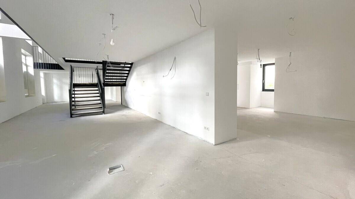 Heller, offener Raum mit Betonboden, weißen Wänden und einer modernen schwarzen Treppe.
