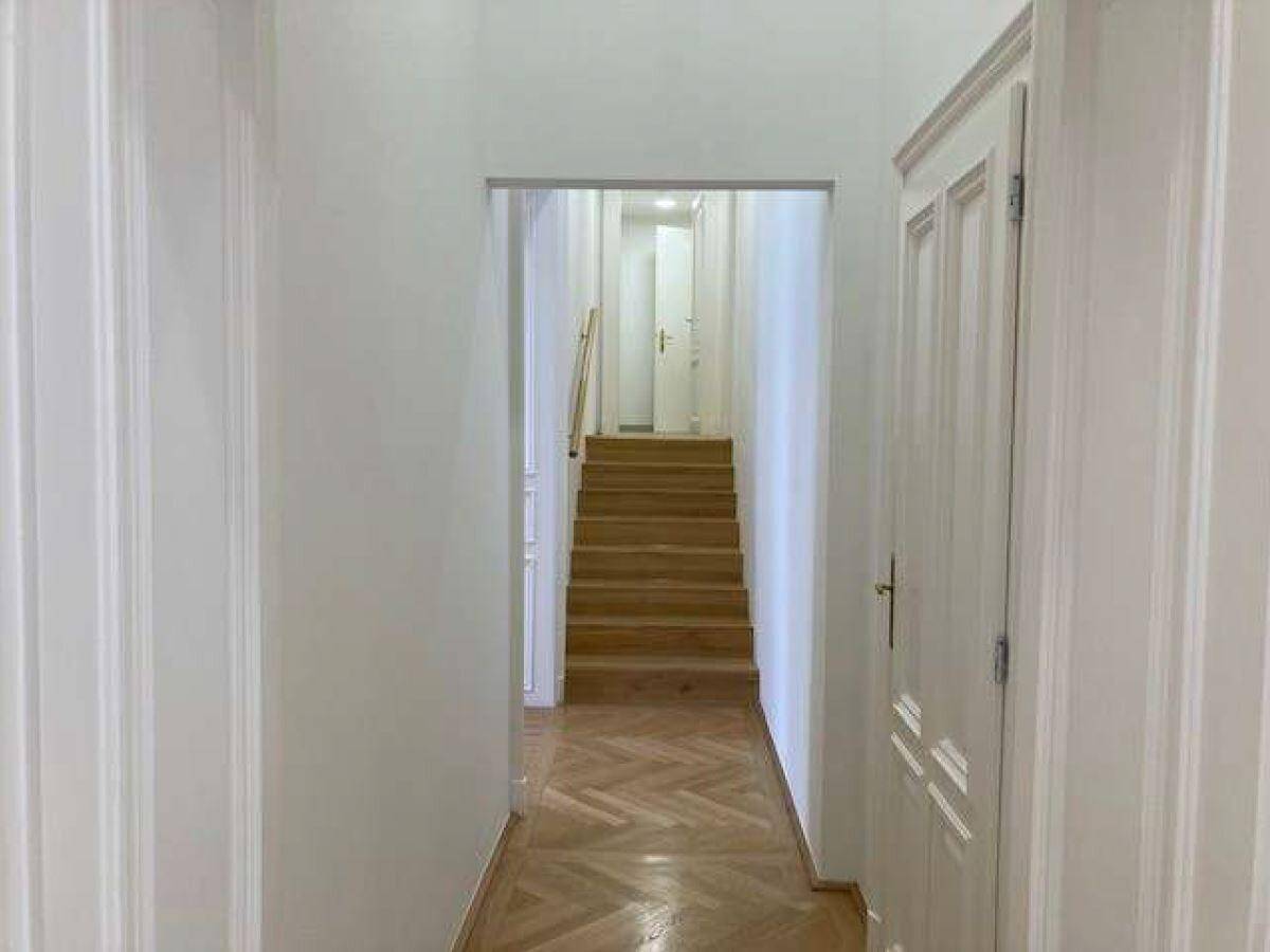 Langer Flur mit hellem Fischgrätparkett und einer eleganten Holztreppe, die in die oberen Stockwerke führt.