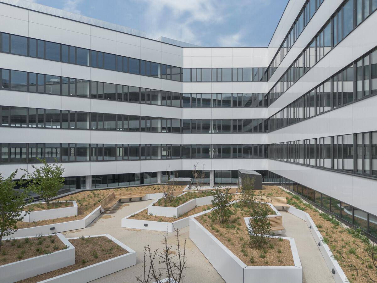 Begrünter Innenhof eines modernen Bürokomplexes mit Sitzgelegenheiten und minimalistischer Gestaltung.