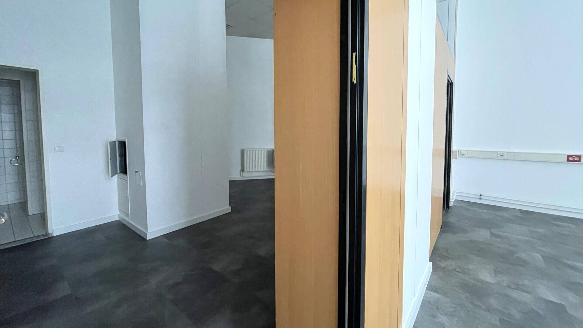 Blick in einen weiteren Bürobereich mit dunklem Boden, weißen Wänden und einem Heizkörper an der Seite.