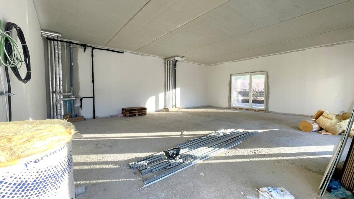 Großer, heller Rohbau-Raum im Erdgeschoss mit großen Fenstern und sichtbaren Installationen.