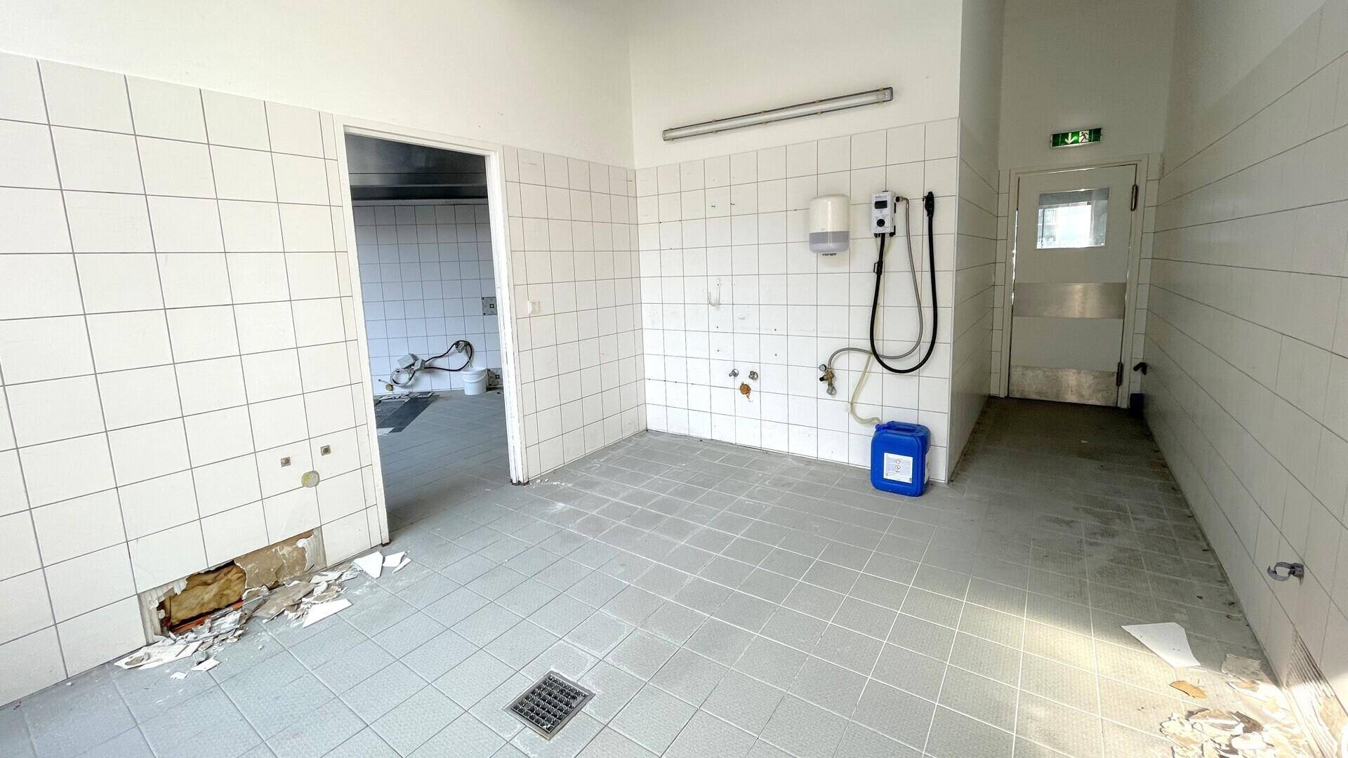 Utility-Bereich in einer Gewerbeküche mit gefliesten Wänden, Bodenablauf und sichtbaren Anschlüssen.