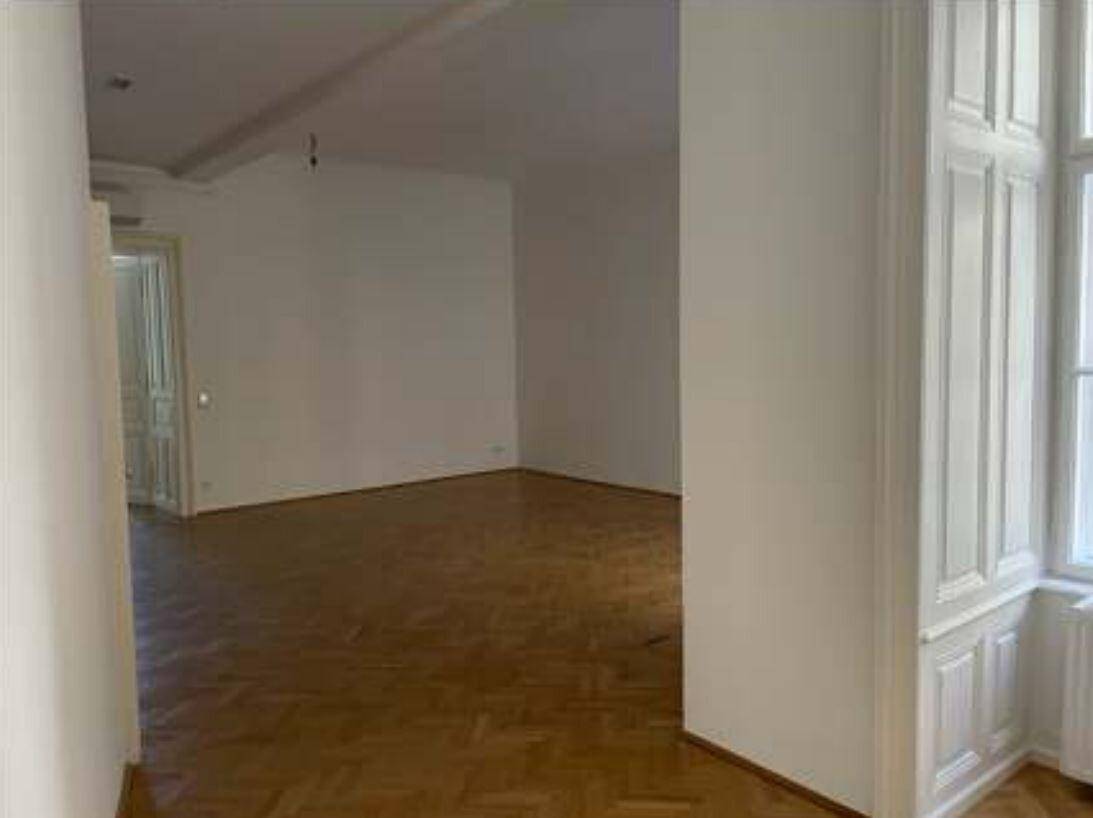 Geräumiger Raum mit Fischgrätparkett und hohen Fenstern, die viel Tageslicht hereinlassen.