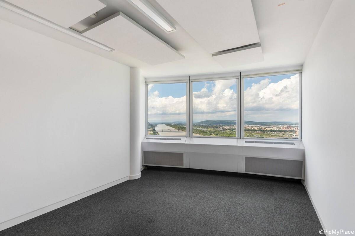 Heller, leerer Büroraum mit Teppichboden, weißen Wänden und großen Fenstern, die einen weiten Ausblick bieten.