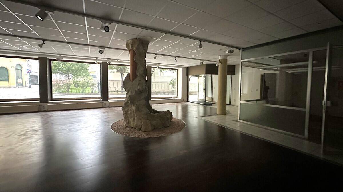 Weitläufiger Geschäftsraum mit dunklem Boden, einer dekorativen Steinsäule und großen Fenstern zum Innenhof.