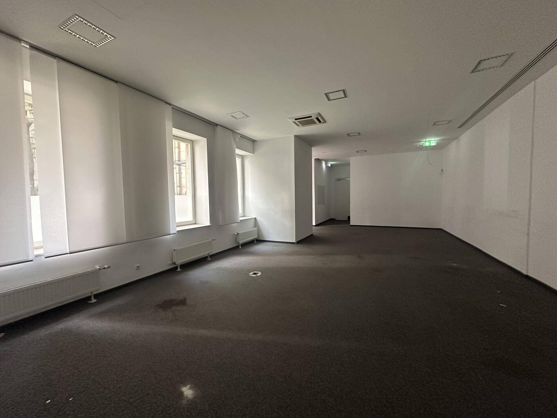 Heller Büroraum mit Teppichboden, großen Fenstern und Heizkörpern unter den Fensterbänken.