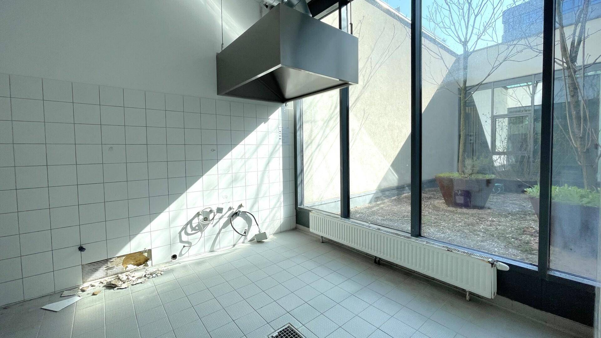 Heller Küchenbereich mit großen Fensterfronten, Blick auf einen Innenhof und sichtbaren Heizkörpern.