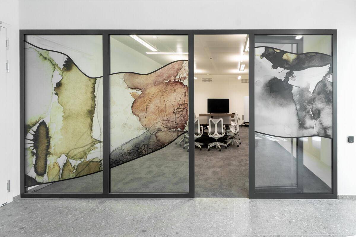 Konferenzraum hinter künstlerisch gestalteten Glastüren mit modernem Interieur und Teppichboden.