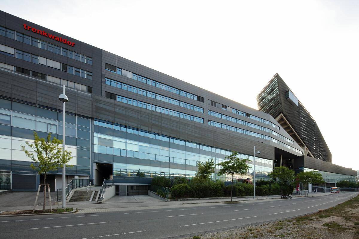 Großes modernes Bürogebäude mit vielen Fenstern und einer Zufahrt von der Straße bei Tageslicht.