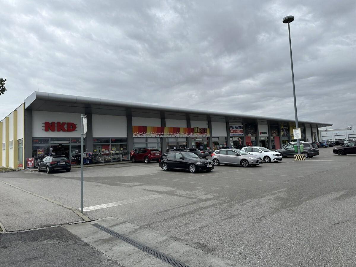 Außenansicht des modernen Geschäftsgebäudes mit breitem Parkplatz und mehreren geparkten Fahrzeugen.