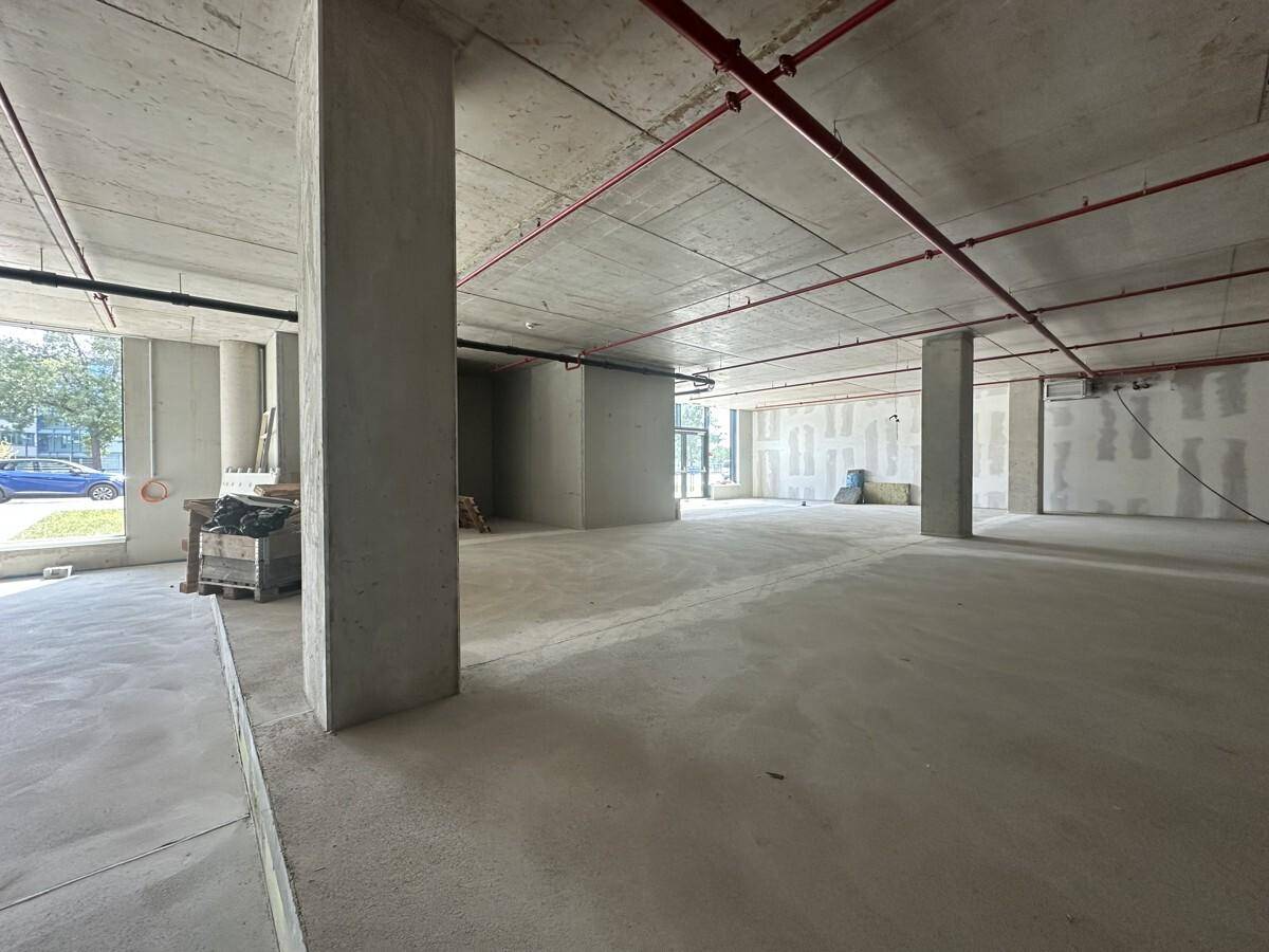Ein weitläufiger, unfertiger Innenraum mit Betonstützen und großen Fenstern zur Straßenseite.