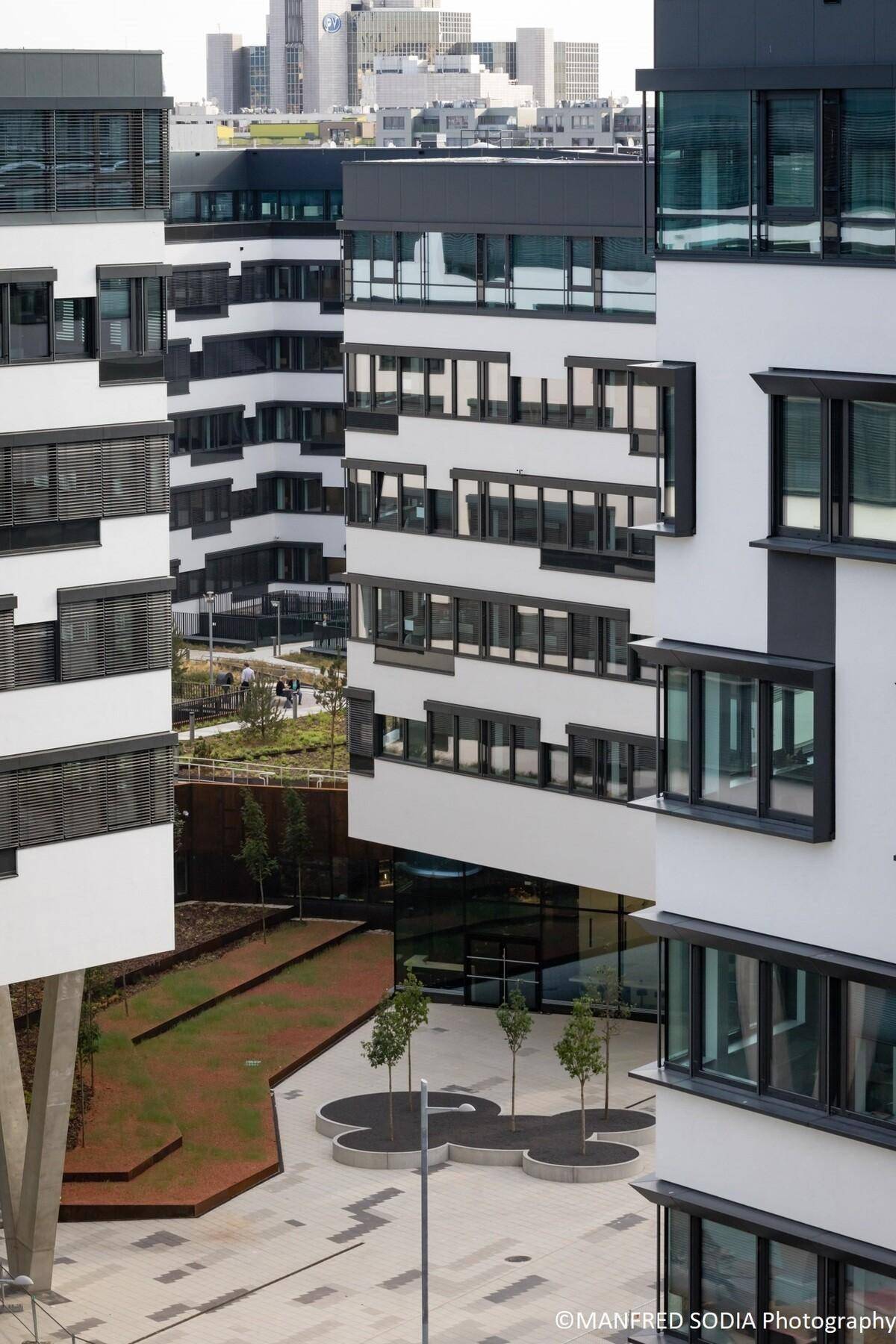 Blick von oben auf moderne Bürogebäude mit gestuften Fassaden und begrünten Außenbereichen in einer städtischen Umgebung.