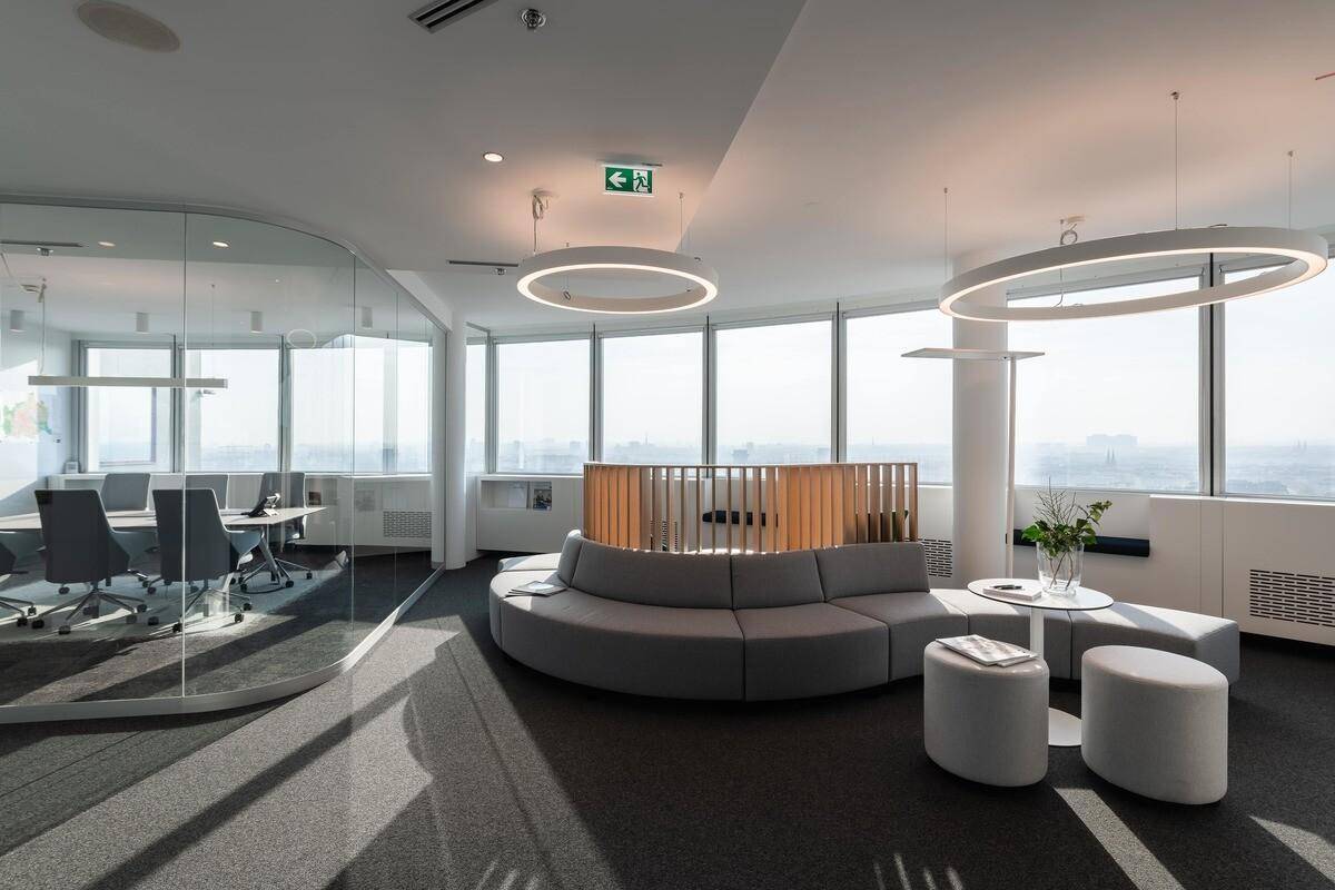 Heller Bürobereich mit großen Fenstern, runden Sofas und einem Konferenzraum hinter Glaswänden.
