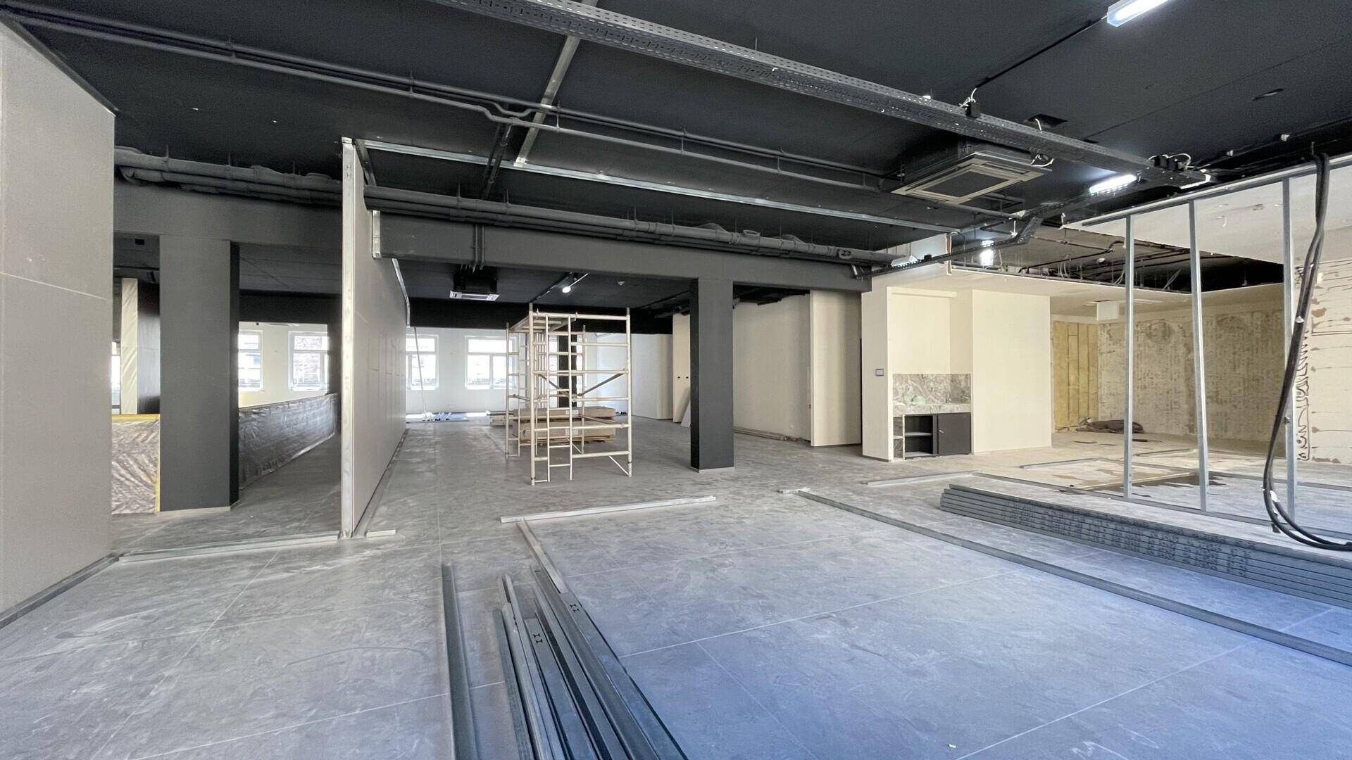 Offener Bürobereich im Bau mit sichtbaren Deckeninstallationen und vorbereiteten Wänden.